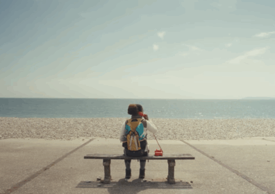 black woman on a bench on a beach holding a red telephone looking out to sea