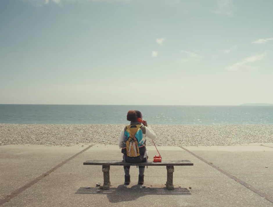 Rural Racism Project black woman on a bench on a beach holding a red telephone looking out to sea