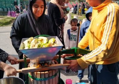 apple power apple juicer with woman in hijab behin dit two people hold the juicer steady